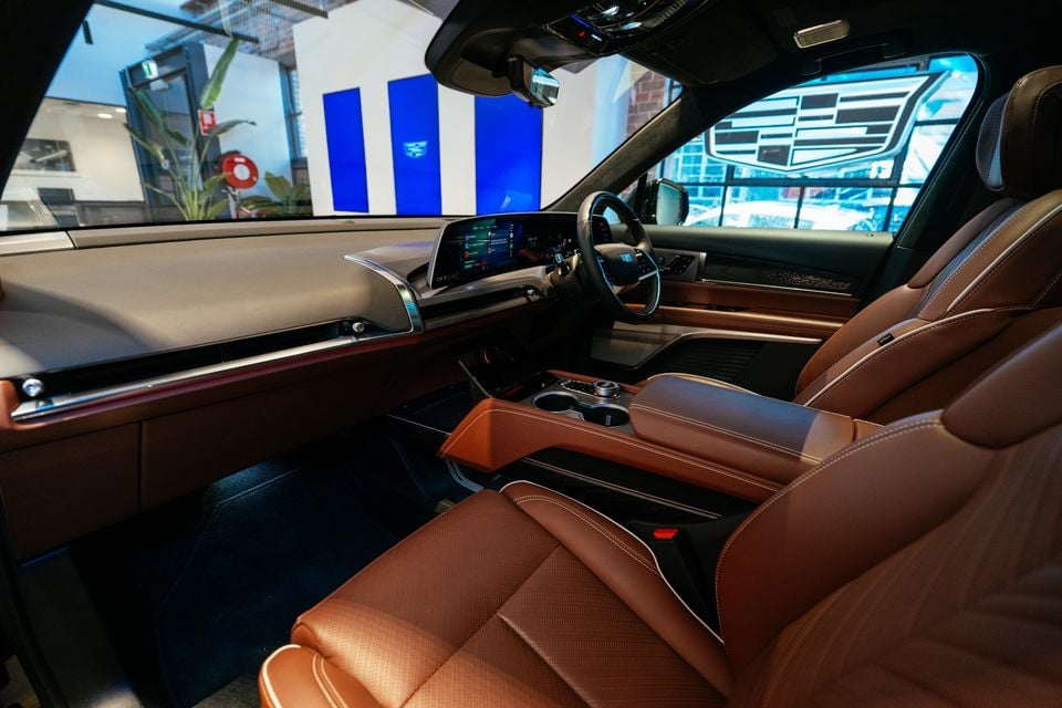 Interior of a 2026 Cadillac VISTIQ Platinum showing tan leather front seats, centre console, and large infotainment screen, viewed from the passenger side