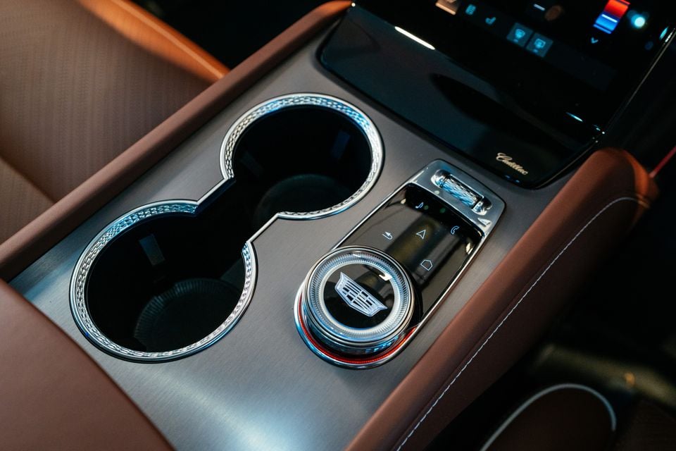 Cadillac Vistiq centre console showing illuminated cup holders, a rotary dial with Cadillac badge, and control buttons with tan leather trim
