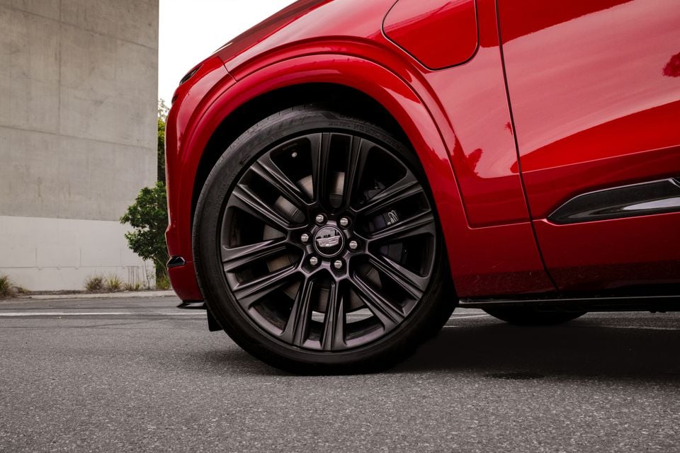 Close-up low-angle view of a black alloy wheel on a red Cadillac XT6 SUV, showing the Cadillac badge on the wheel centre cap