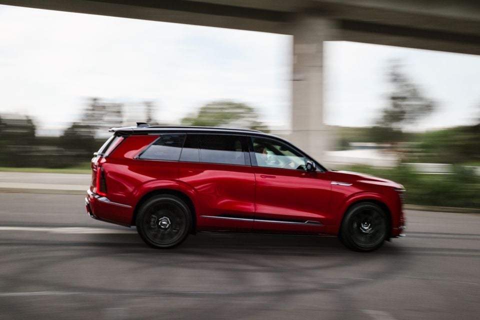 A red 2026 Cadillac Vistiq large SUV seen from the side while driving on a road beneath an overpass