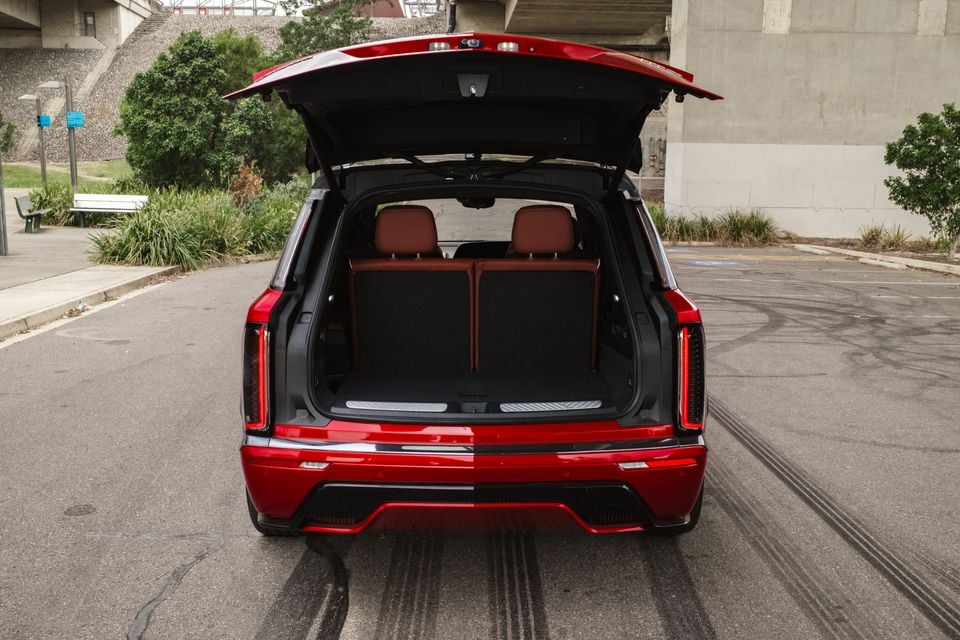 Red 2026 Cadillac XT6 SUV seen from the rear with the powered tailgate open, showing the empty boot and red leather rear seats