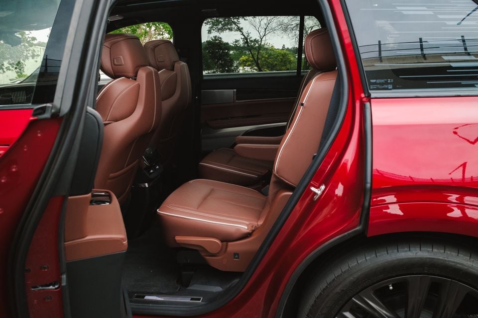 Interior view of a red 2026 Cadillac Vistiq showing tan leather second-row captain's chairs with white contrast stitching, viewed through an open rear door