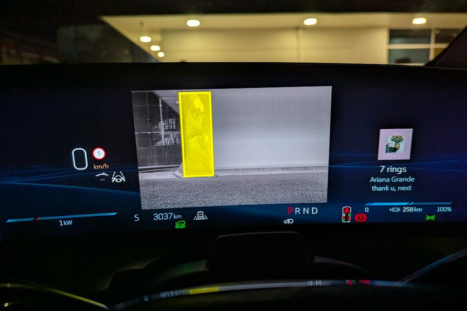 Cadillac VISTIQ digital instrument cluster displaying a night vision camera feed with a pedestrian highlighted in yellow, alongside speed, range, and music playback information