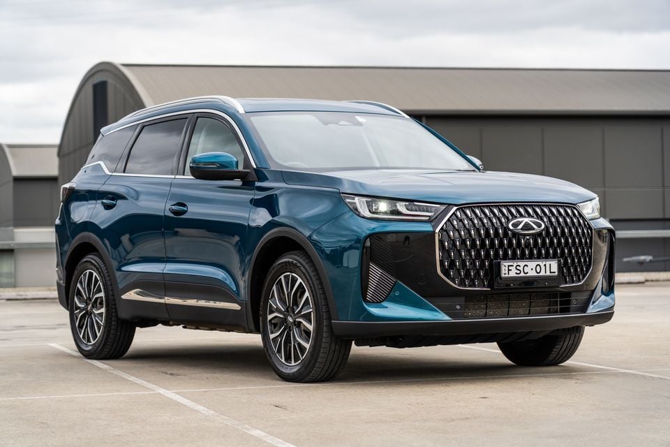 A teal 2026 Chery Tiggo 7 Super Hybrid SUV seen from the front-left side, parked in an open area with an industrial building in the background.