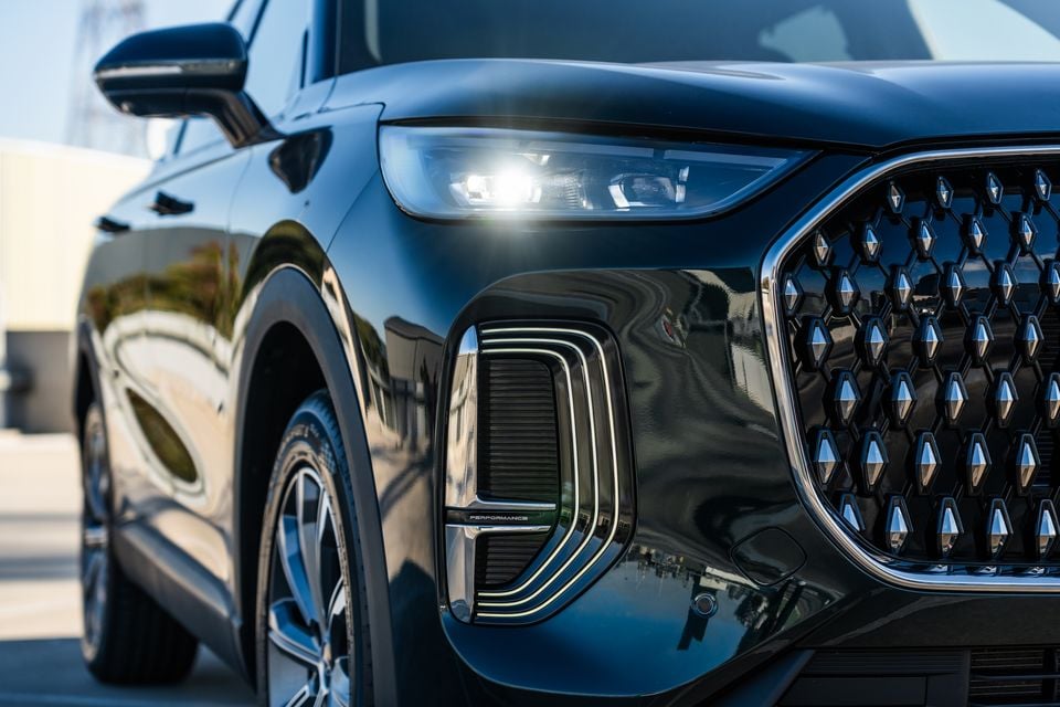 Close-up of the front corner of a dark blue 2026 Chery Tiggo 9 Super Hybrid SUV, showing the large diamond-pattern grille, LED headlight, and front bumper intake
