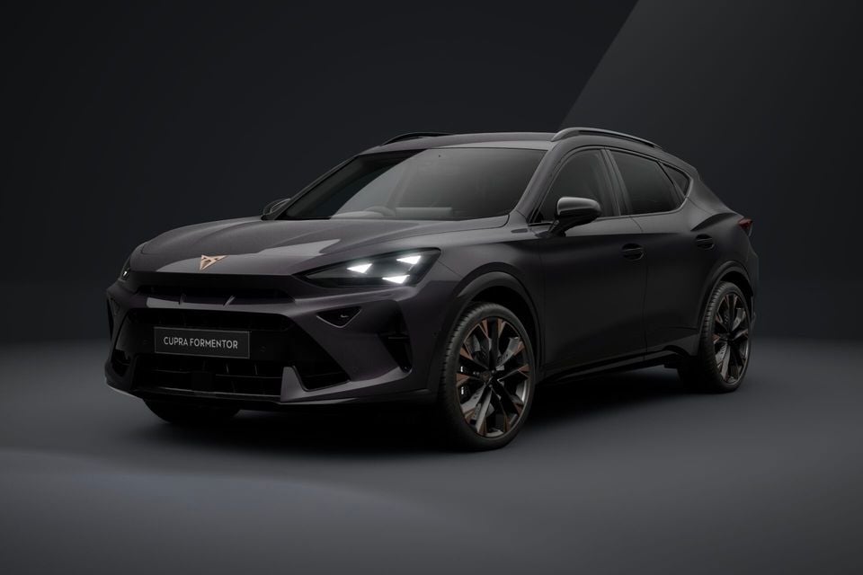 A dark grey 2026 Cupra Formentor SUV photographed from the front three-quarter angle in a studio setting, with headlights illuminated and bronze-accented alloy wheels.