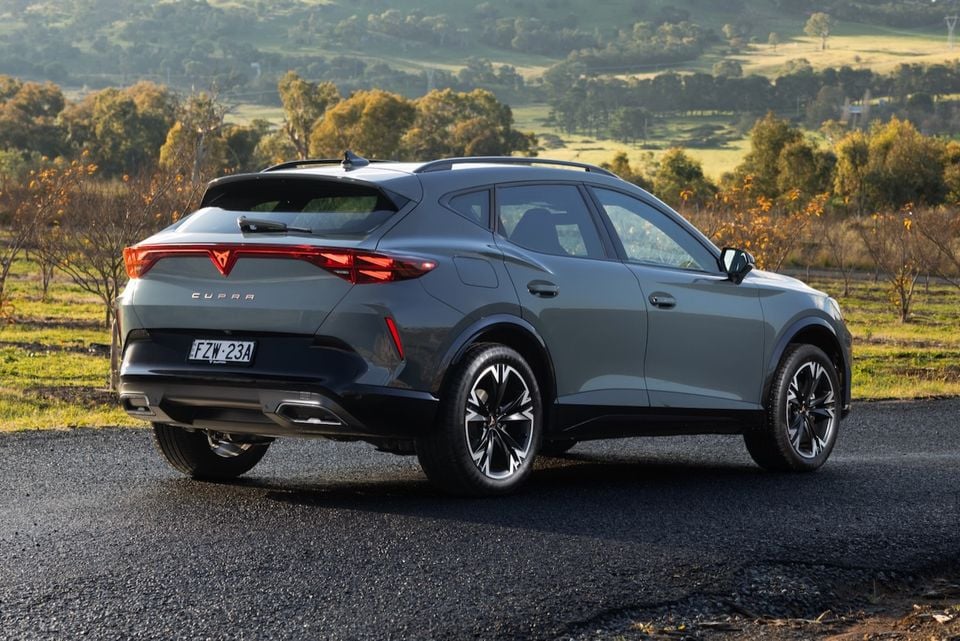 A grey 2026 Cupra Formentor S SUV seen from the rear three-quarter angle, parked on a rural road with rolling countryside in the background