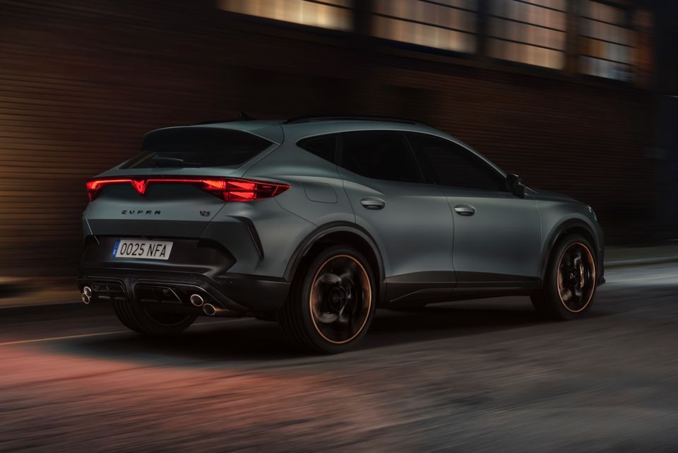 A grey 2026 Cupra Formentor VZ5 SUV seen from the rear three-quarter angle while driving on a street at night, showing distinctive taillights and dual exhaust tips.