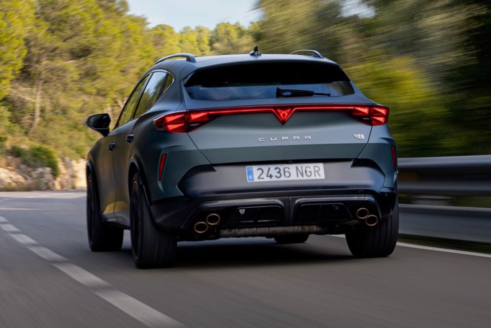 Rear view of a dark green Cupra Formentor VZ5 SUV driving on a road, showing quad exhausts and full-width tail-lights