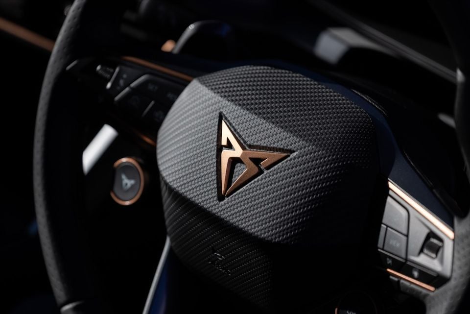 Close-up of the Cupra logo on a carbon-fibre-textured steering wheel with copper accents