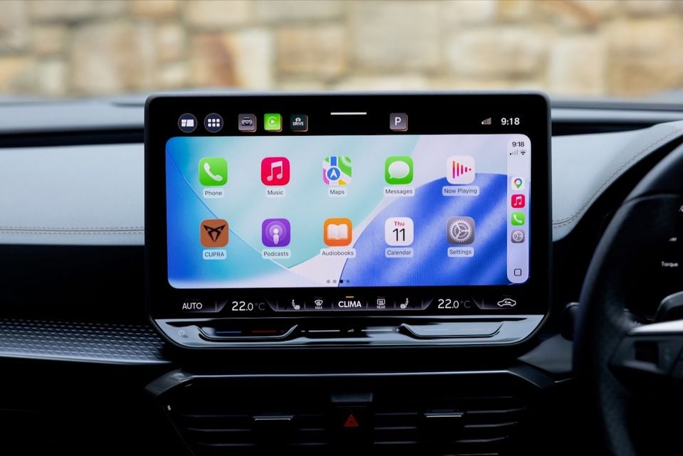 Apple CarPlay home screen displayed on the infotainment touchscreen of a Cupra Formentor, showing apps including Phone, Music, Maps, Messages, Podcasts and Settings, with dual-zone climate controls below