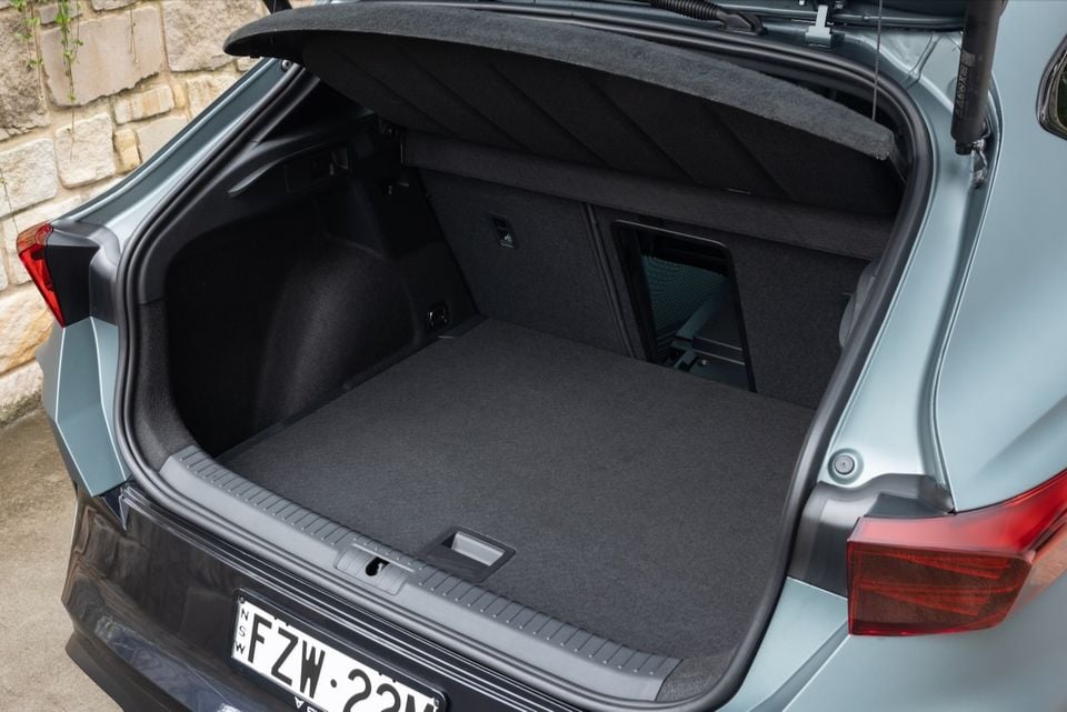 Boot interior of a light blue 2026 Cupra Formentor VZX SUV, open and empty with carpeted floor and a side storage compartment visible