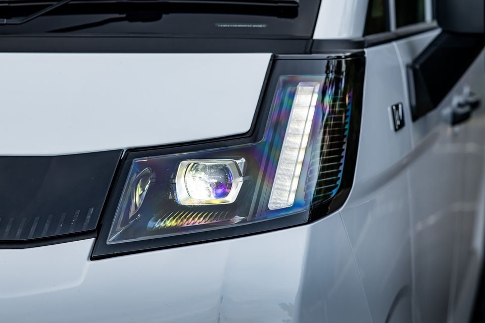 Close-up of the LED headlight on a white 2026 Farizon V7E, showing iridescent projector lens and daytime running light strip
