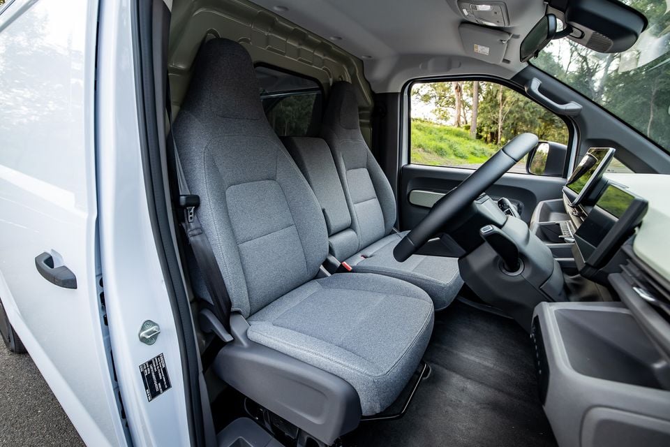Interior view of a 2026 Farizon V7E van showing the front cabin with grey fabric bench seats, steering wheel, and infotainment screen
