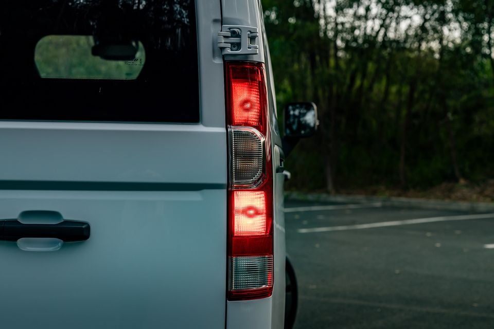 Close-up of the rear tail light on a white van, with trees visible in the background