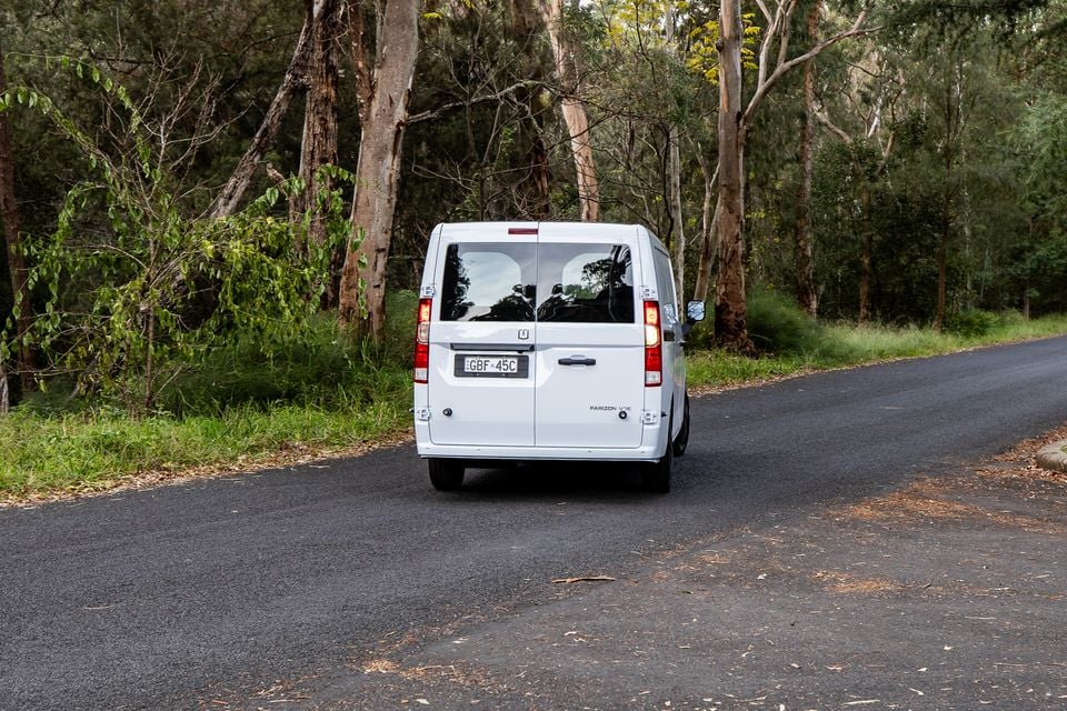 A white Farizon V7E van seen from the rear, driving along a tree-lined road in Australia.