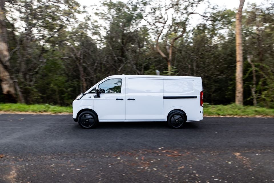 A white Farizon V7E electric van driving along a tree-lined road, seen from the side