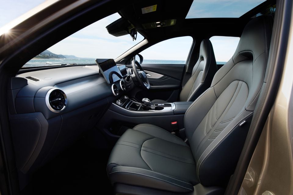 Interior view of a 2026 Forthing Taikon 5 showing the front seats, centre console, touchscreen infotainment display, and circular air vents, with an ocean view through the windscreen