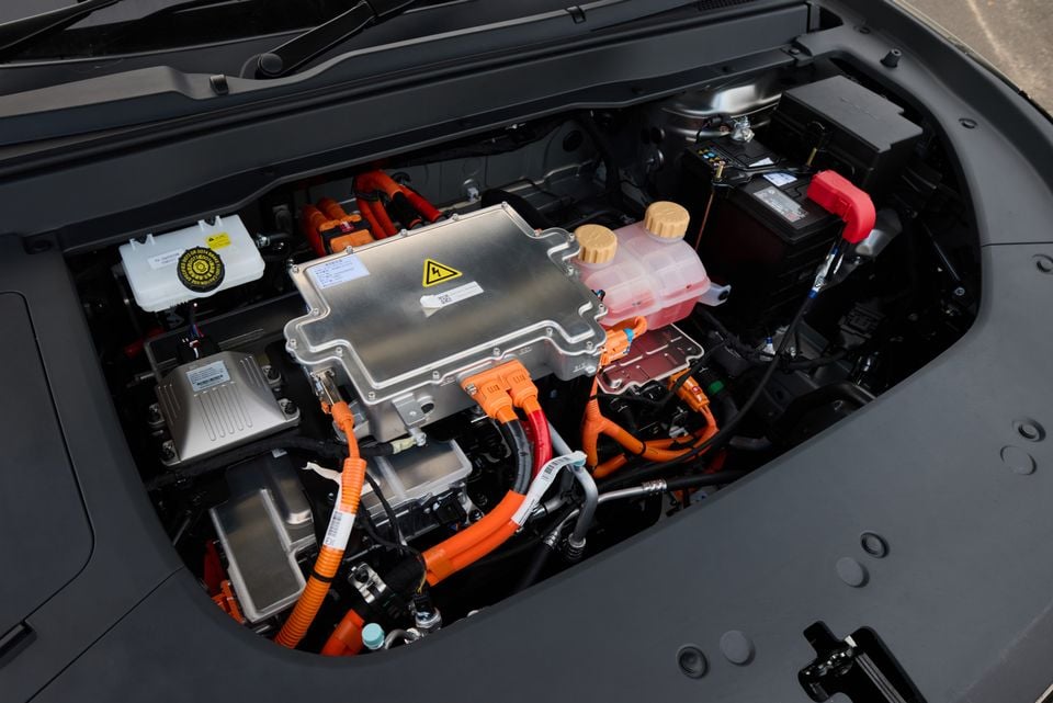 The electric motor bay of a Forthing Taikon 5, showing orange high-voltage cables, a power inverter unit with a high-voltage warning label, and auxiliary components under an open bonnet.