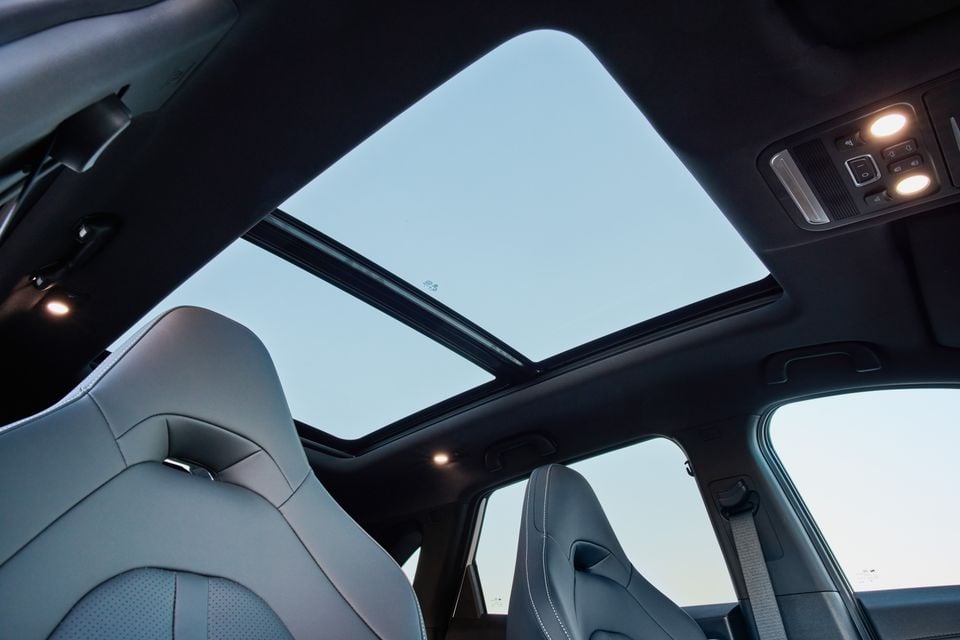 Interior view of a car looking up at a large panoramic sunroof, with grey leather seats and overhead controls visible