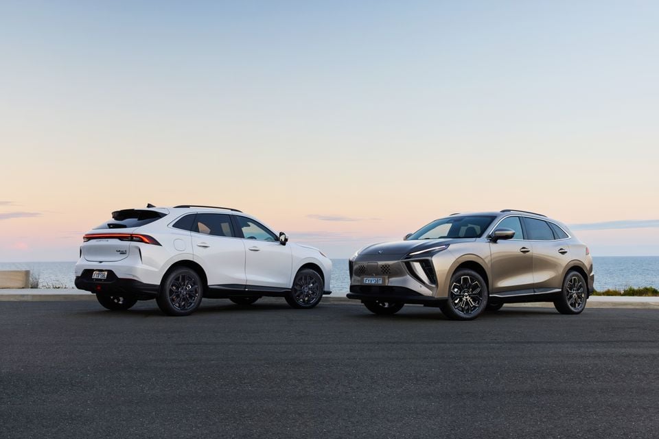 Two Forthing Taikon 5 SUVs parked side by side near the coast at dusk, one in white seen from the rear and one in gold seen from the front