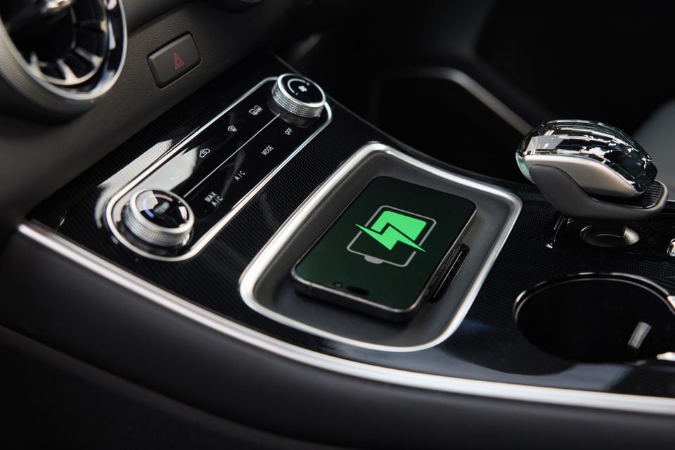 A smartphone sitting on the wireless charging pad in a car's centre console, displaying a wireless charging icon