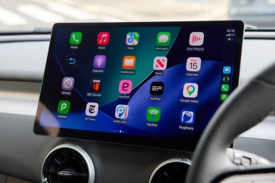 Apple CarPlay interface displayed on the touchscreen infotainment system of a car, showing apps including Maps, Google Maps, Music, Podcasts, PlugShare and PayStay