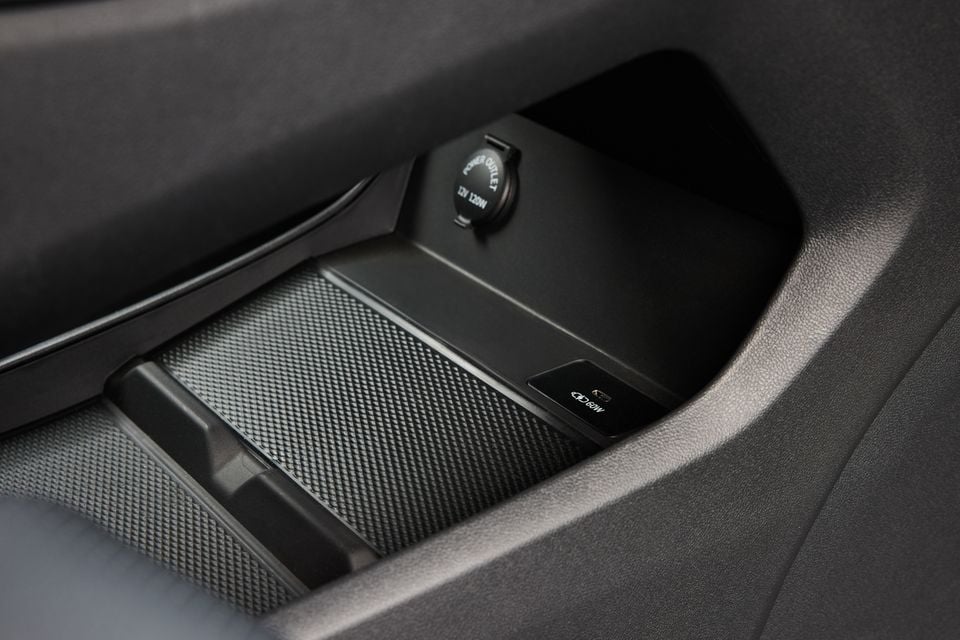 Close-up of a car interior storage area showing a 12V 120W power outlet and a wireless charging pad with a button nearby