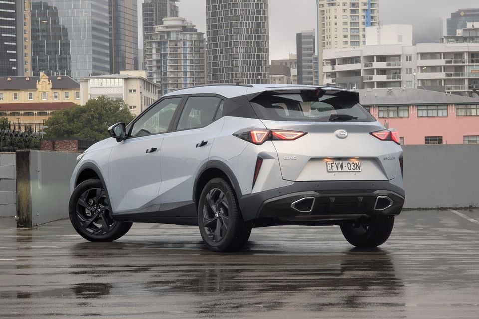 A silver 2026 GAC Emzoom SUV seen from the rear three-quarter angle on a wet rooftop car park with a city skyline in the background