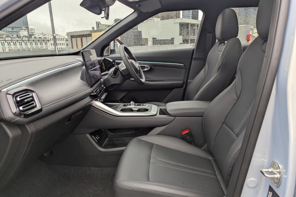 Interior of a GAC Emzoom showing the front seats, centre console, touchscreen infotainment display, and steering wheel, viewed through the open passenger door