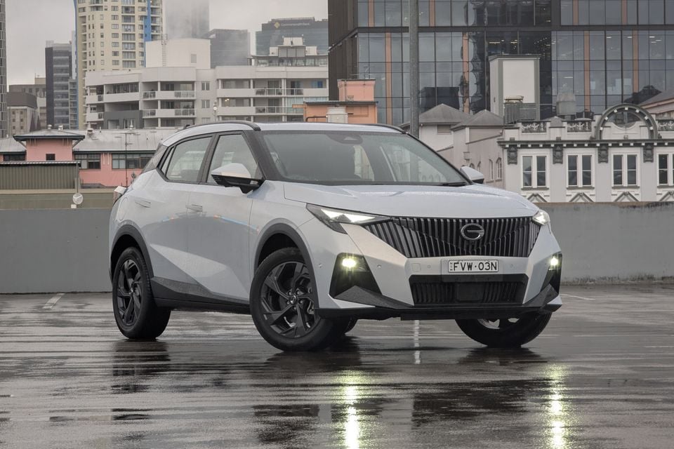 A silver 2026 GAC Emzoom SUV photographed from the front-side angle on a wet rooftop car park with a city skyline in the background