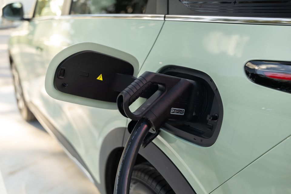 A charging cable plugged into the charge port of a light green electric vehicle