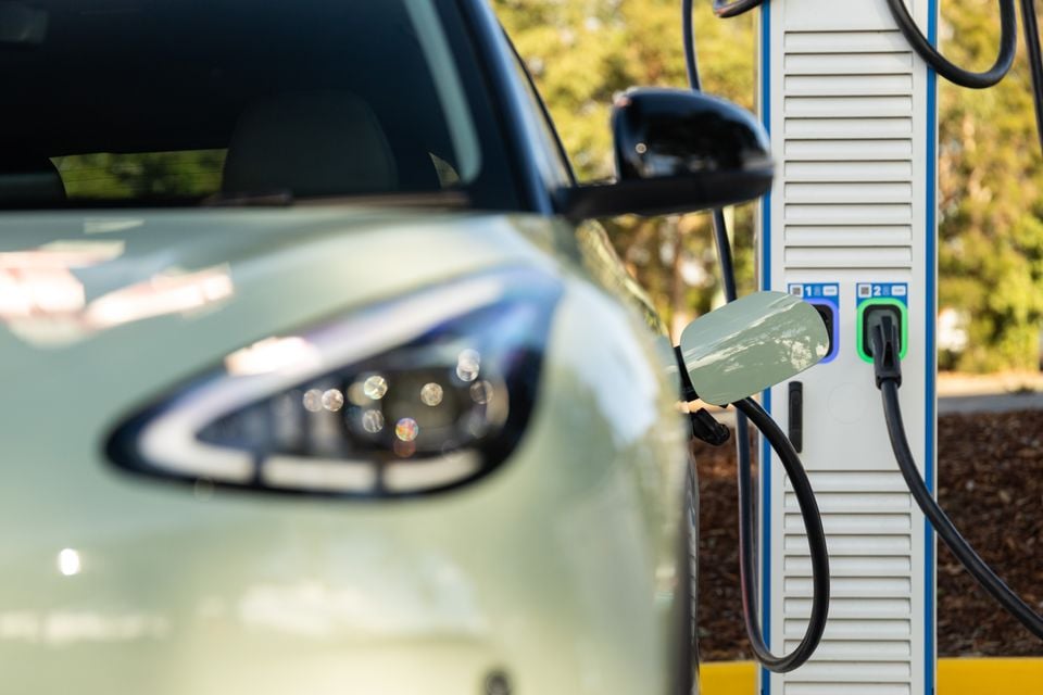 A light green Geely EX2 electric SUV parked at a public DC fast-charging station, shown from the front side with a charging cable connected