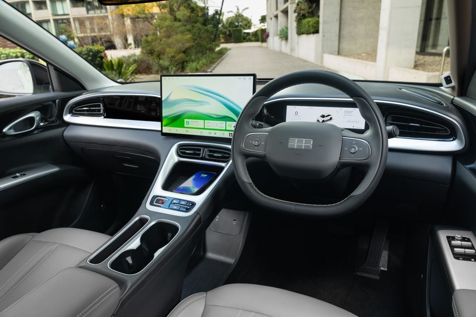 Interior of a 2026 Geely EX2 Inspire showing the dashboard, large central touchscreen infotainment display, digital instrument cluster, steering wheel, and centre console with wireless charging pad