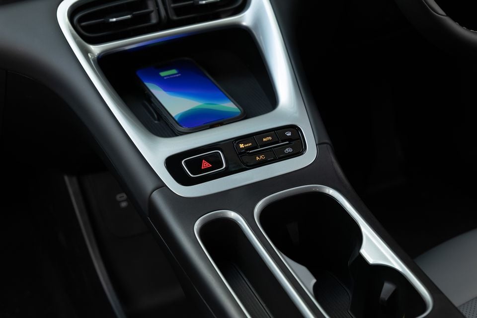 Interior centre console of the 2026 Geely EX2 Inspire showing a wireless phone charger with a smartphone, hazard light button, climate control shortcut buttons, and cup holders