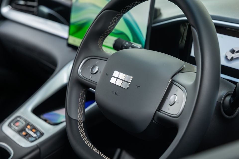 Close-up of the Geely EX2 Inspire steering wheel showing the brand logo, control buttons, and touchscreen infotainment display in the background