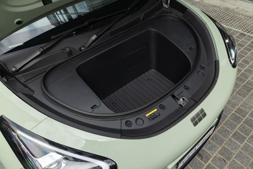 Open front storage compartment (frunk) of a light green Geely EX2, viewed from above showing the empty black plastic storage bin
