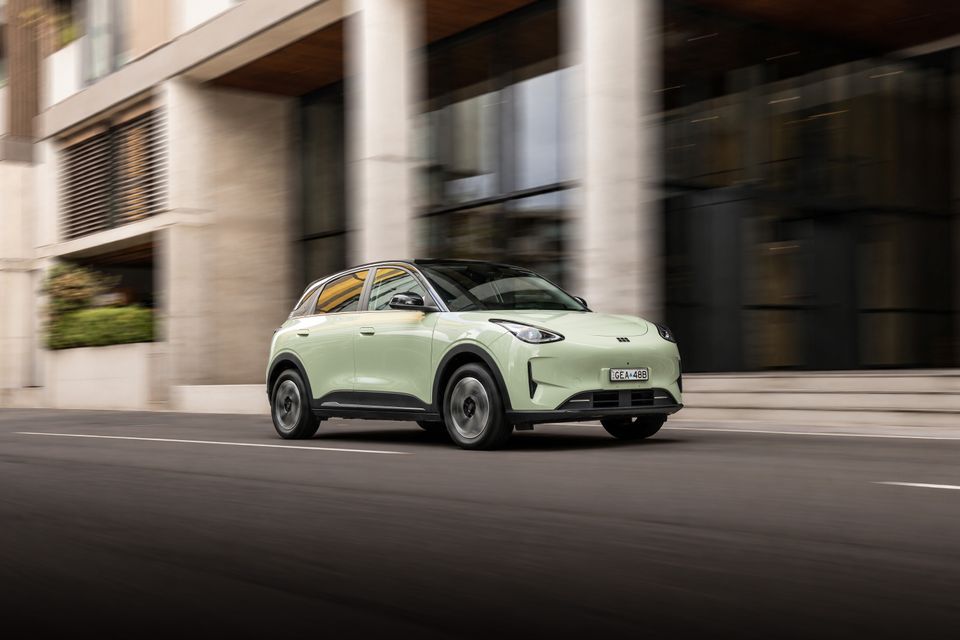 A light green 2026 Geely EX2 Inspire small SUV driving along a city street, seen from the front and side