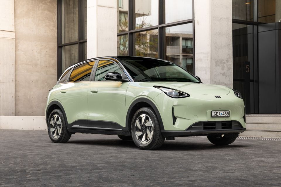Um pequeno SUV Geely EX2 Inspire verde claro 2026 estacionado em frente a um prédio moderno, visto do lado frontal esquerdo