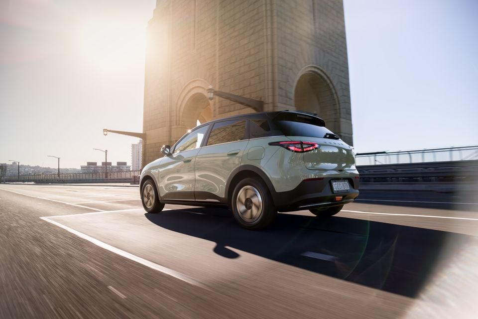 A light green 2026 Geely EX2 small SUV seen from the rear three-quarter angle while driving across a bridge at sunset