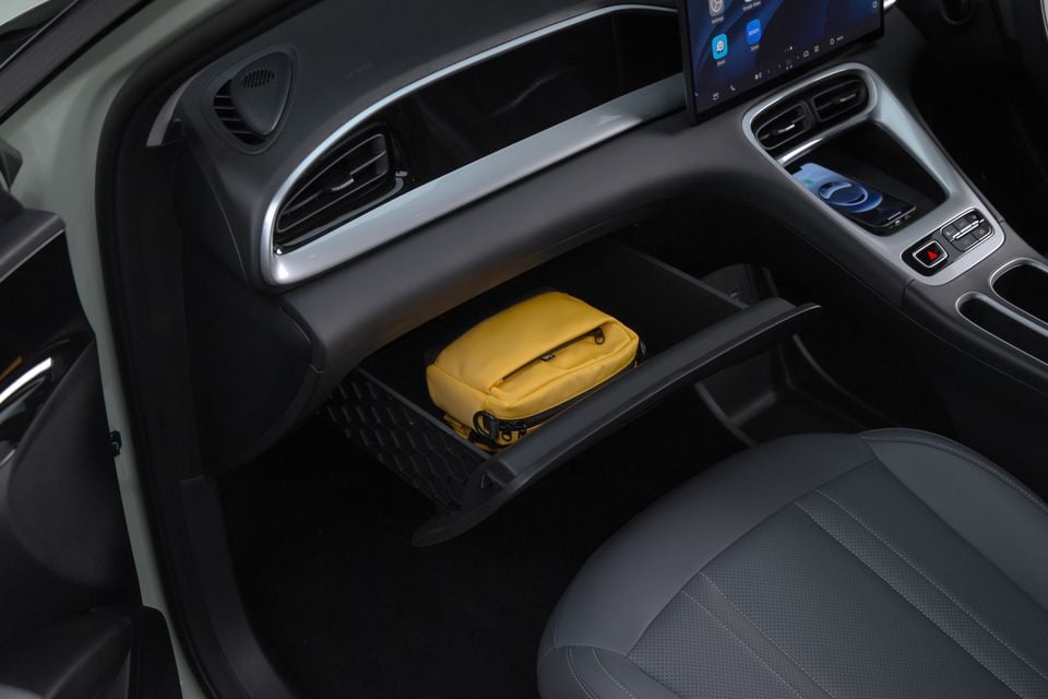 Interior view of a car showing an open under-dash storage shelf with a yellow pouch resting inside, with the touchscreen infotainment display and wireless charging pad visible above