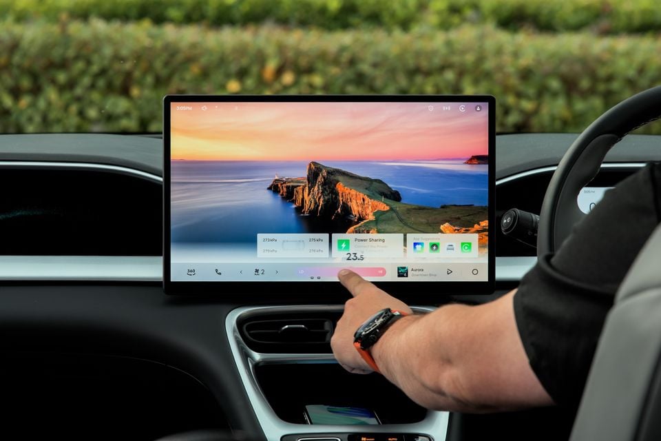 A person touching the large central touchscreen infotainment display inside a Geely EX2 Inspire, showing a scenic landscape wallpaper and various widgets