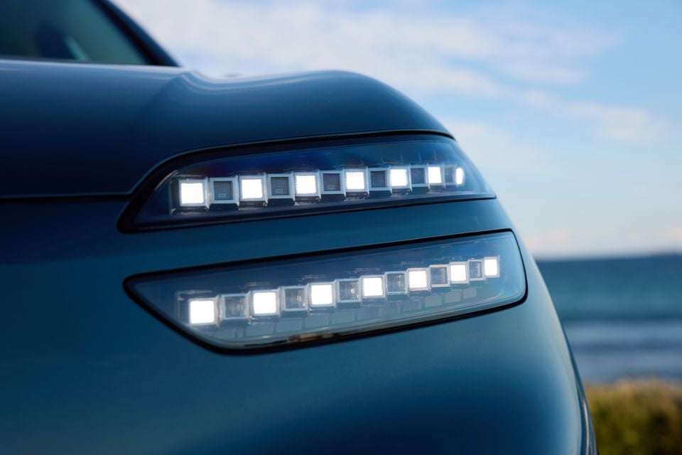 Close-up of the LED headlights on a blue 2026 Genesis GV60, showing illuminated square LED modules across two stacked light strips