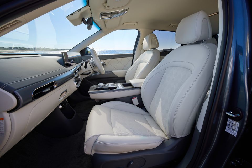 Interior of a 2026 Genesis GV60 showing white leather front seats, centre console and dashboard with a coastal view through the windows