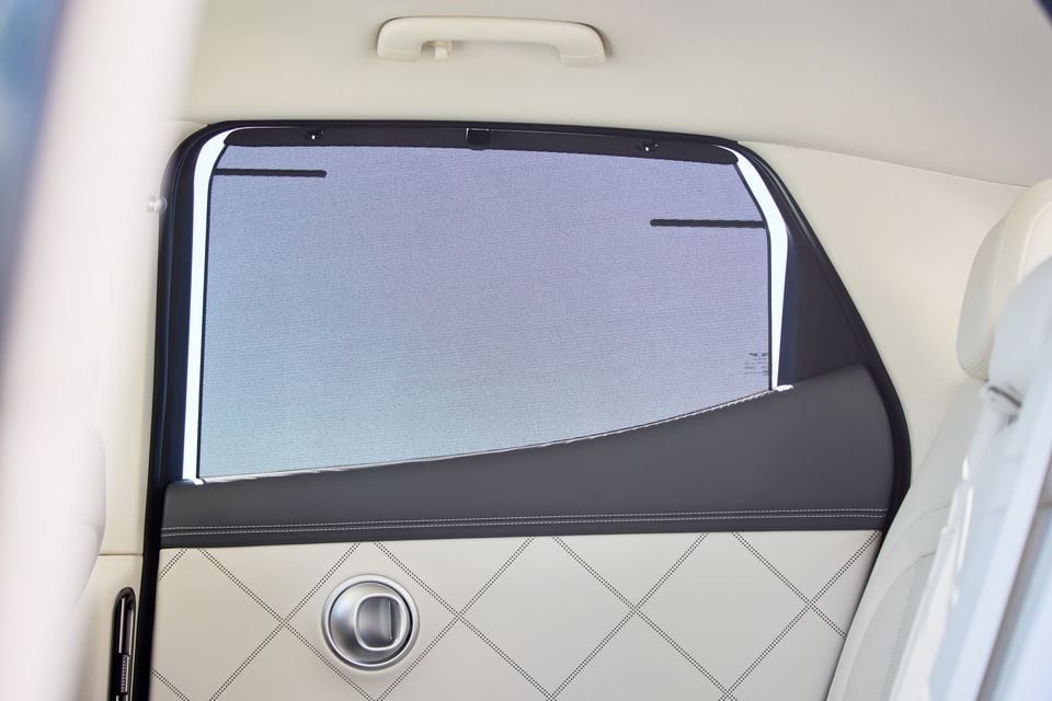Rear passenger door interior of the 2026 Genesis GV60, showing a retractable window sunshade, quilted leather door trim, and chrome door handle