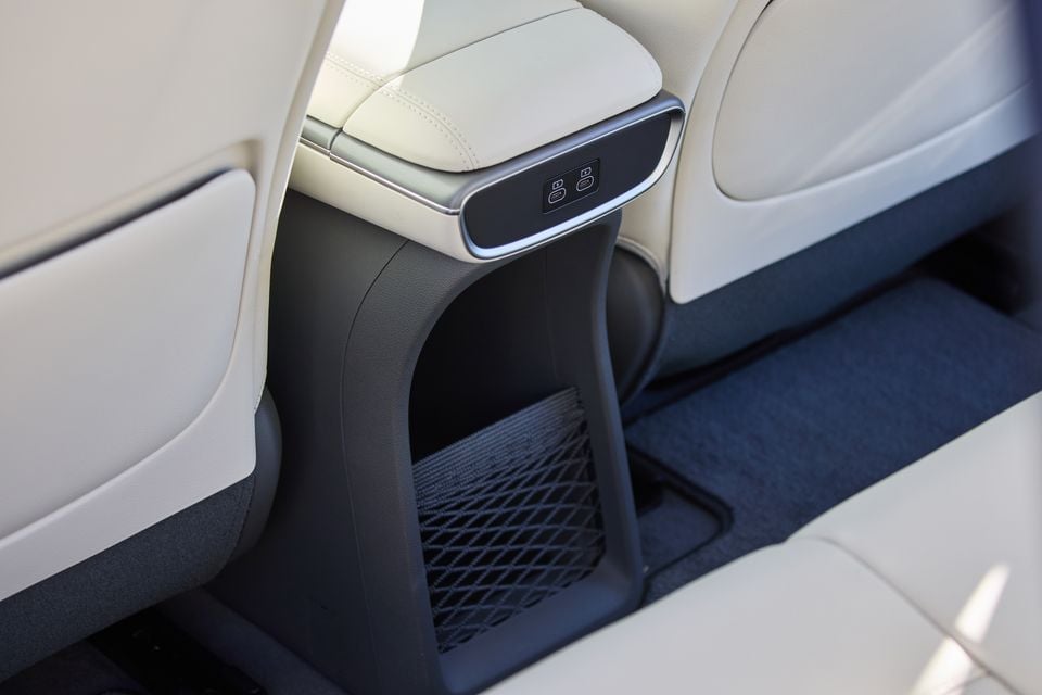 Rear centre console of the 2026 Genesis GV60 showing USB charging ports, a storage net, and light-coloured leather seating trim
