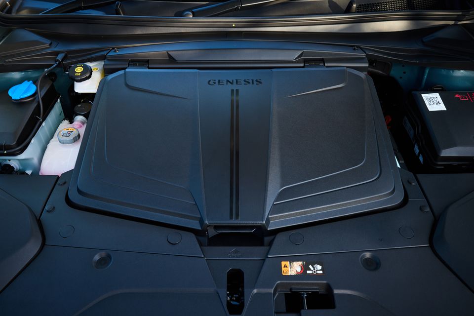 Genesis-branded engine bay cover of a 2026 Genesis GV60, with fluid reservoirs and battery visible alongside.