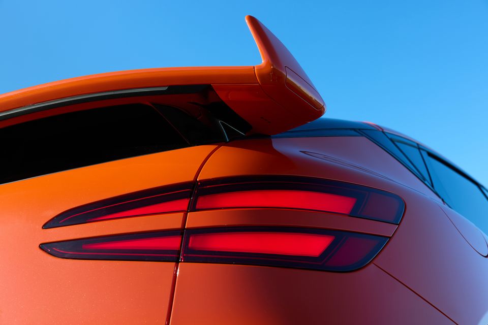 Close-up of the rear tail light and spoiler on an orange 2026 Genesis GV60 Magma against a blue sky