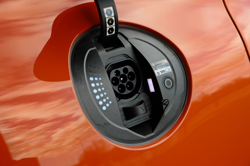 Close-up of the electric vehicle charging port on an orange 2026 Genesis GV60 Magma, showing a Type 2 AC inlet with CCS combo socket