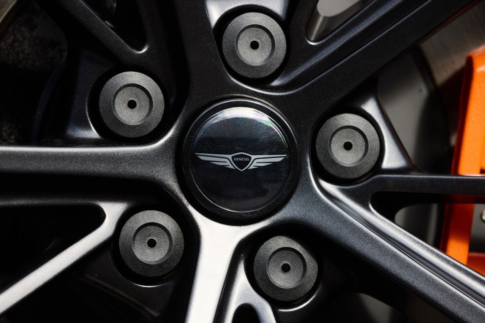 Close-up of a Genesis alloy wheel centre cap with the Genesis winged logo, with an orange brake caliper visible in the background
